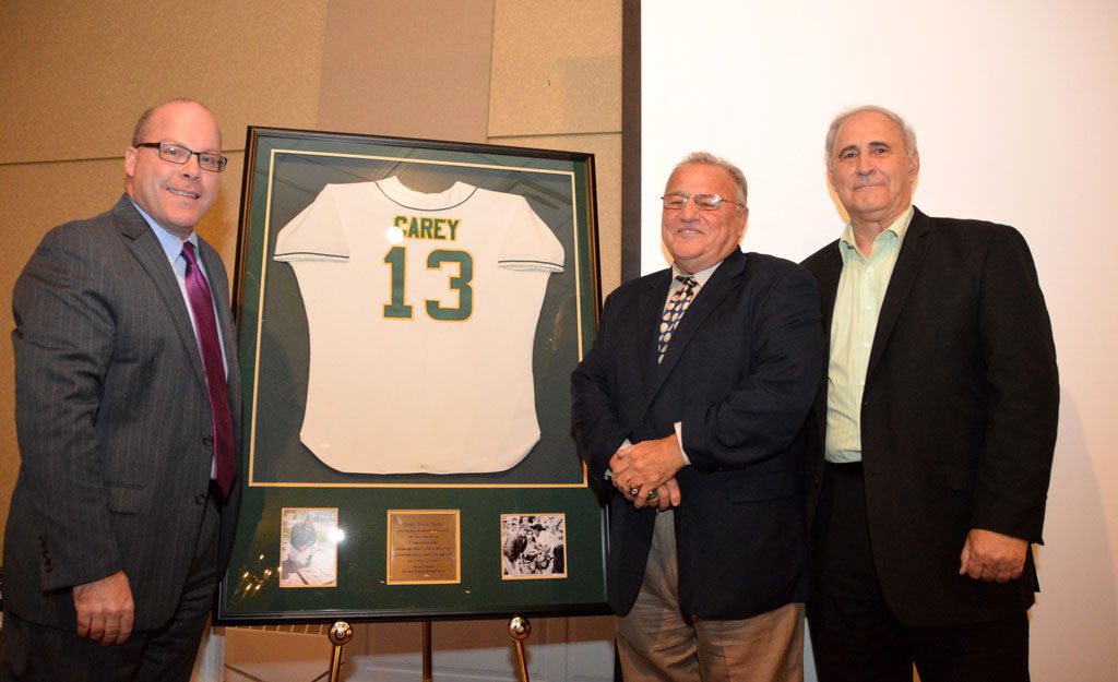A UNIQUE HONOR. The School Committee voted to formally retire baseball coach Frank Carey's uniform number on the occasion of his retirement party. Carey has stepped down as coach after 47 years. Above, Supt. Jon Bernard, (left), and school board Chairman Jerry Venezia, (right), unveil Carey's retired jersey. (Bob Turosz Photo)