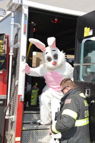 FIRE CAPTAIN ERIC PEPPER assists the world–famous Easter Bunny in alighting from a Fire Department engine at the Batchelder School field, where he was greeted by crowds of thrilled children. (Bob Turosz Photo)
