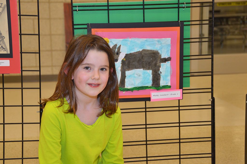 BATCHELDER SCHOOL second grader Maddy Lambert is shown next to her art on exhibit in the high school, part of a display of student art from throughout the district, from elementary to high school, sponsored by the visual arts department. (Bob Turosz Photo)