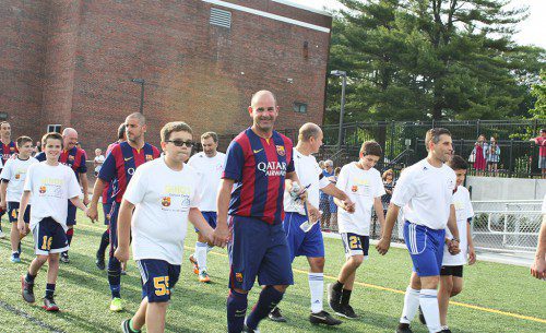 PLAYERS from the visiting F.C. Barcelona team (striped jerseys) held hands with local youth soccer players who served as their escorts as they entered Pioneer Stadium with their Boston Braves counterparts (white jerseys) at Thursday's game. (Maureen Doherty Photo)