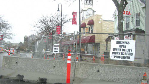 A SECTION of downtown sidewalk where new utility conduits are being installed is fenced off with signs announcing that businesses remain open during the utility work. Signs also point to additional parking on Main Street. (Mark Sardella Photo)