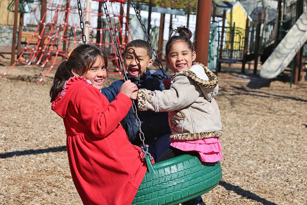 LOCAL CHILDREN, from left, Laysha Crispin, Isaac Solano and Sheylin Crispin had a blast on the tire swing at Hesseltine playground last weekend. (Donna Larsson Photo)