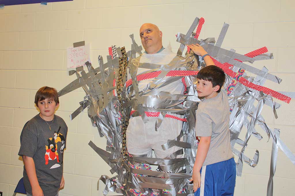 SIXTH GRADERS Anthony Carol (left) and Connor Preston put on the finishing touch after sixth graders duct taped Middle School Principal Stephen Ralston to the wall during lunch April 13. The event raised over $1,000 for the Lynnfield Middle School PTO. (Dan Tomasello Photo)