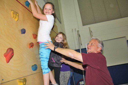 RETIRING Summer Street School physical education teacher Craig Stone assists second graders Addison Munion (left) and Zoe Rockwell up the elementary school’s rock wall April 14. (Dan Tomasello Photo)